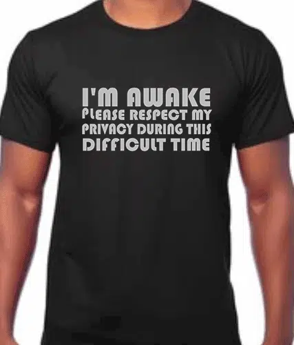 Image of a blackcotton t shirt with funny slogan "I'm awake please respect my privacy during this difficult time" printed in white on the front.